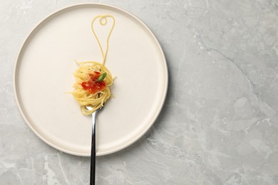 Photo of Heart made with spaghetti and fork on grey table, top view. Space for text