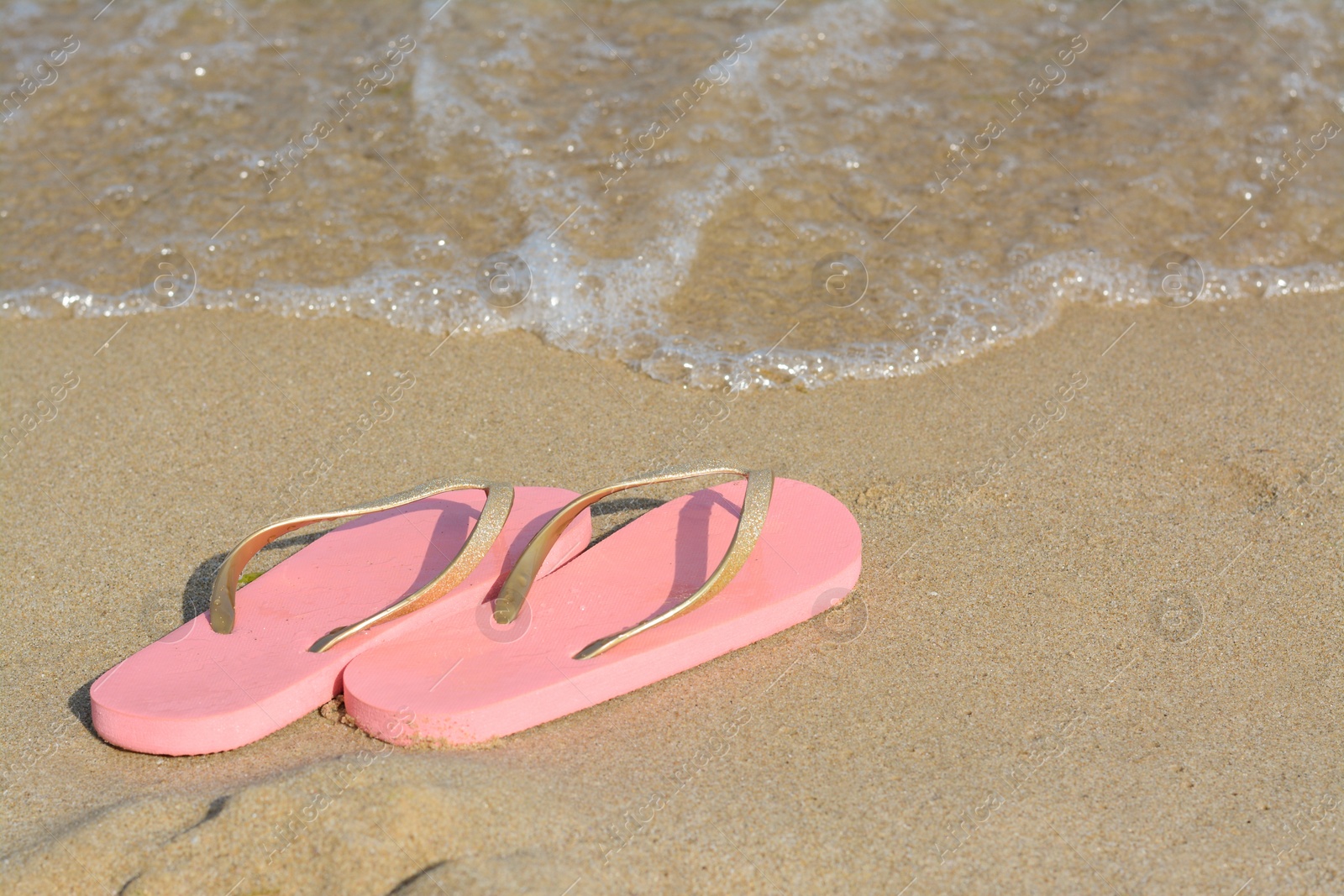 Photo of Stylish flip flops on sandy beach near sea