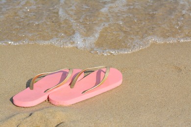 Stylish flip flops on sandy beach near sea