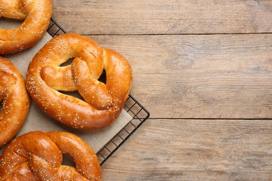 Cooling rack with delicious freshly baked pretzels on wooden table, top view. Space for text