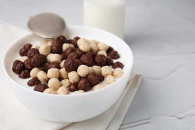 Breakfast cereal. Tasty corn balls with milk in bowl and spoon on white textured table, closeup. Space for text