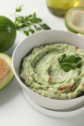 Delicious guacamole and ingredients on white table