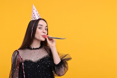 Photo of Woman in party hat with blower and streamers on orange background, space for text
