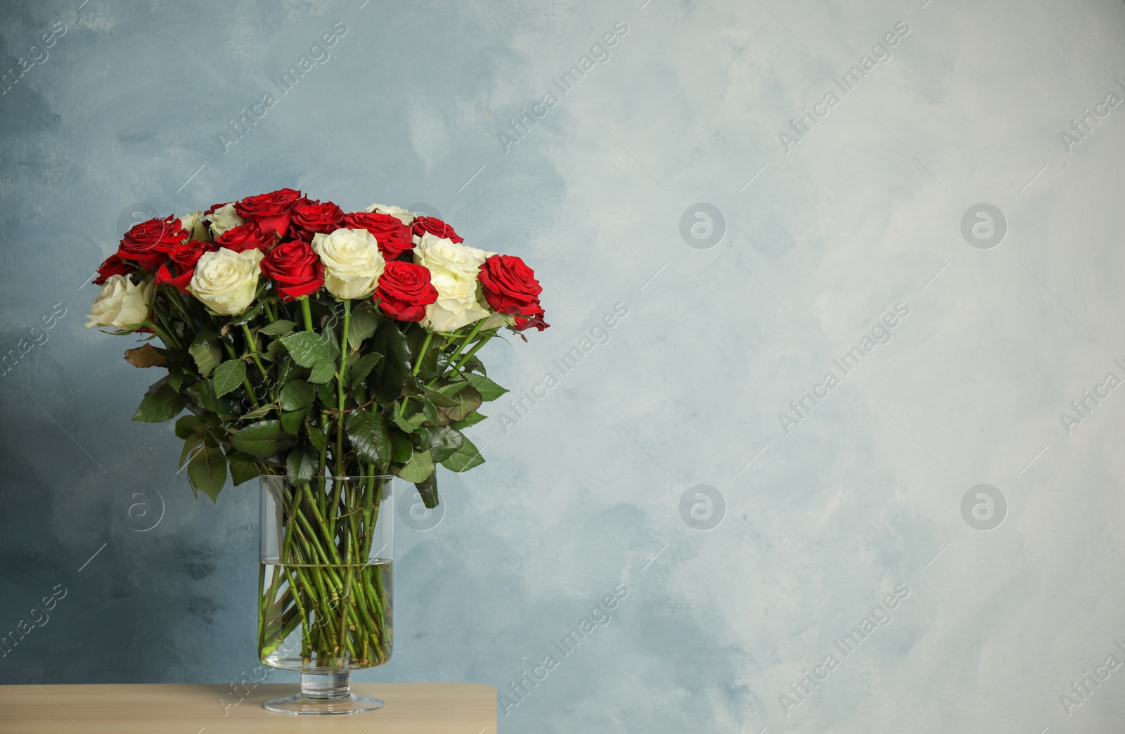 Photo of Luxury bouquet of fresh roses on wooden table. Space for text