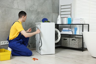 Photo of Young plumber examining drain hose of washing machine in bathroom