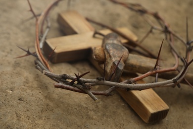 Photo of Crown of thorns, wooden cross and hammer on ground, closeup. Easter attributes