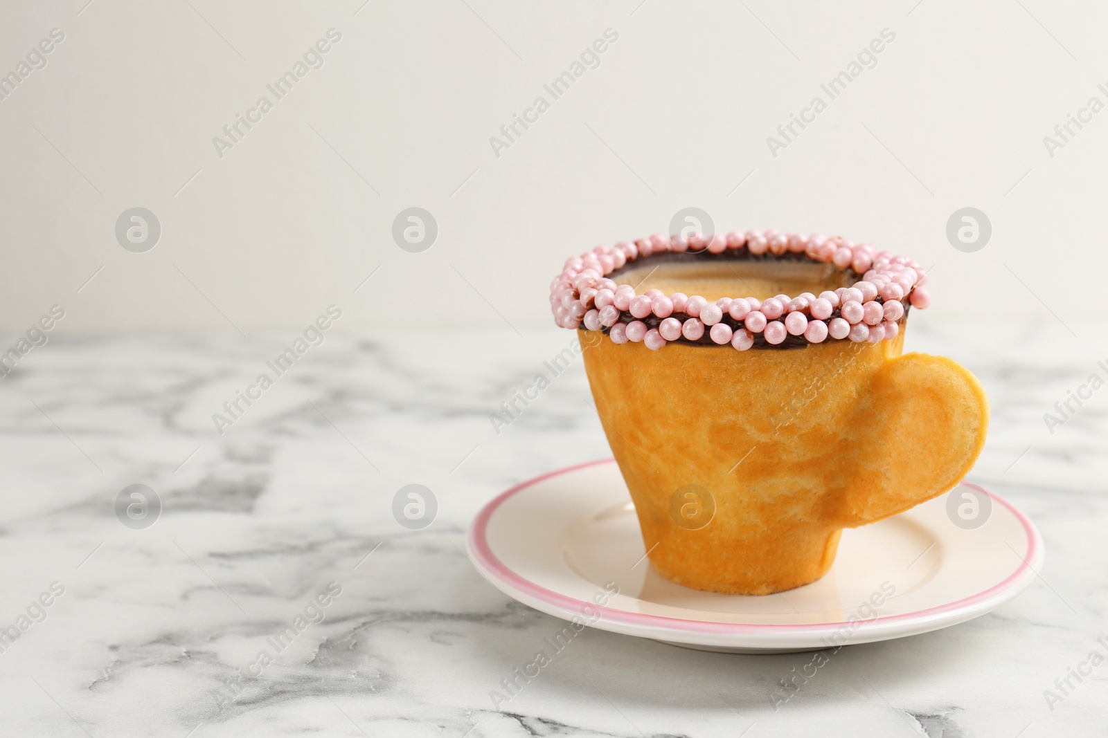 Photo of Delicious edible biscuit cup of coffee decorated with sprinkles on white marble table, space for text