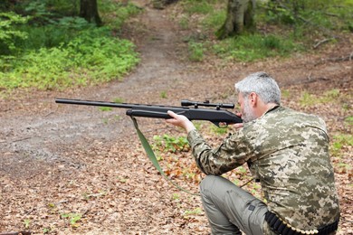 Photo of Man wearing camouflage and aiming with hunting rifle in forest