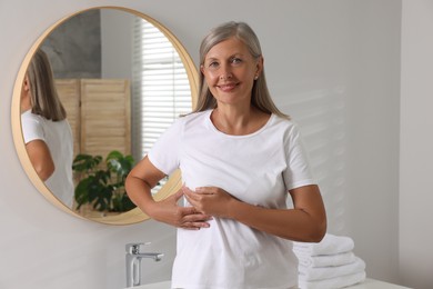 Photo of Beautiful senior woman doing breast self-examination in bathroom