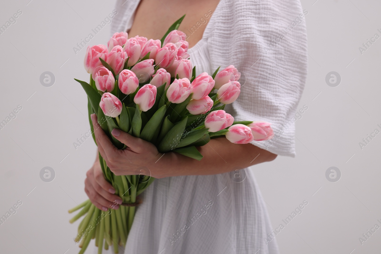 Photo of Woman with bouquet of beautiful fresh tulips on light grey background, closeup