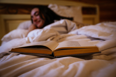 Photo of Woman sleeping in bed at home, focus on open book