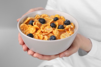 Photo of Woman holding bowl of crispy corn flakes with milk and blueberries, closeup