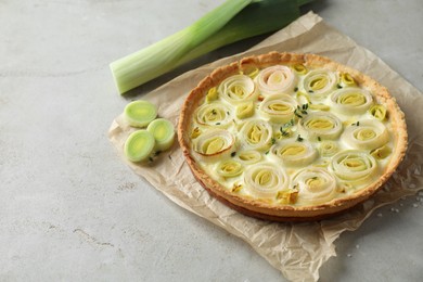 Photo of Tasty leek pie and fresh stalk on grey textured table. Space for text