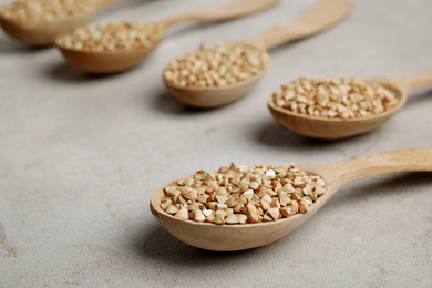 Photo of Uncooked green buckwheat grains in spoons on light table