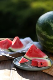 Photo of Slices of ripe watermelon with spoon on wooden table outdoors