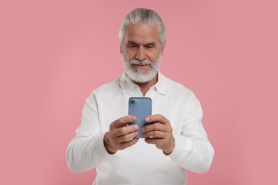 Photo of Senior man using smartphone on pink background
