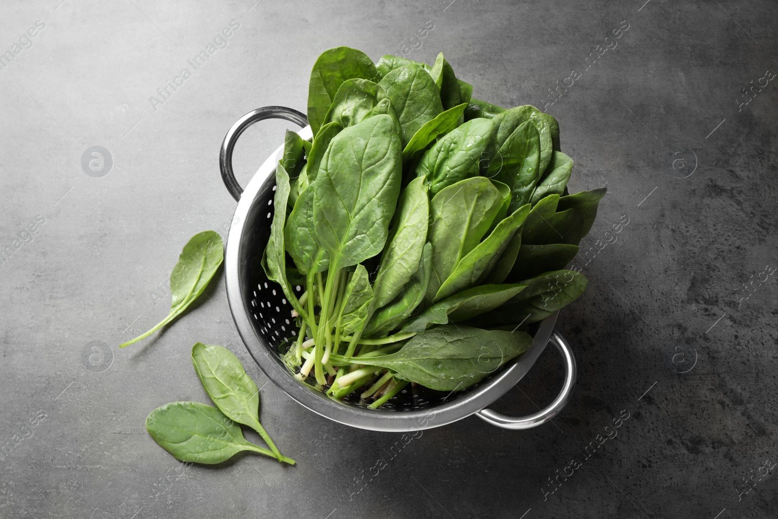 Photo of Colander with fresh green healthy spinach on grey table, flat lay