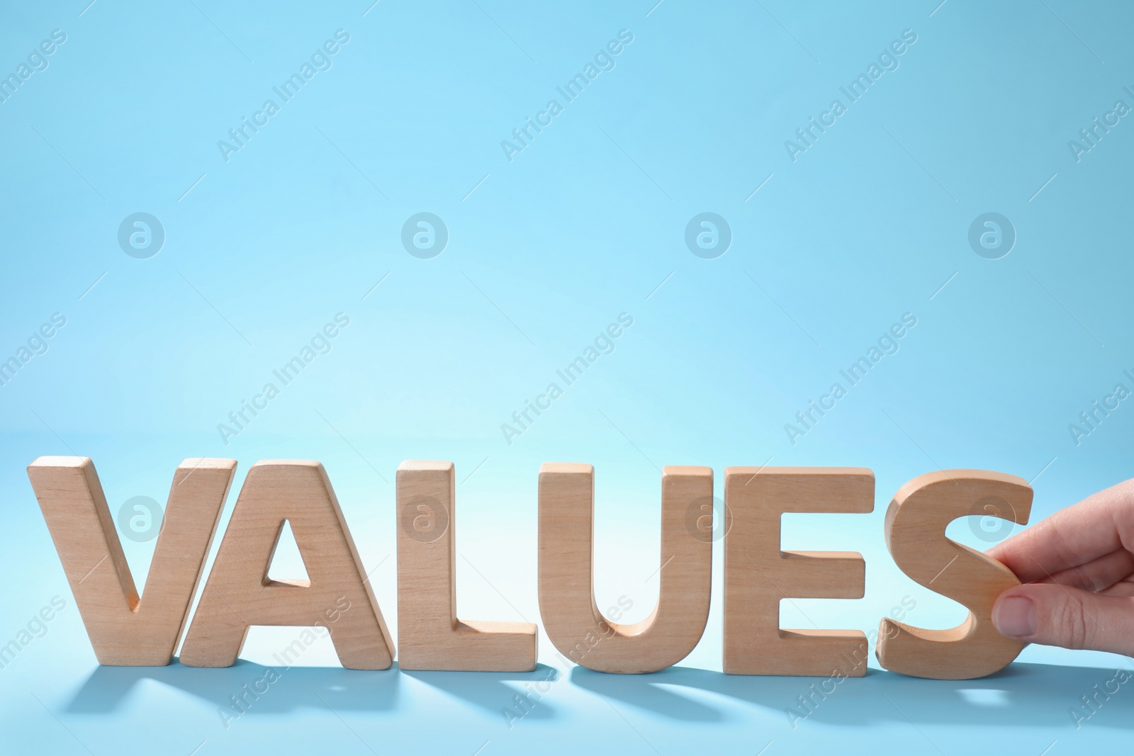 Photo of Woman making word VALUES with wooden letters on light blue background, closeup