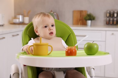 Cute little baby with healthy food in high chair at home