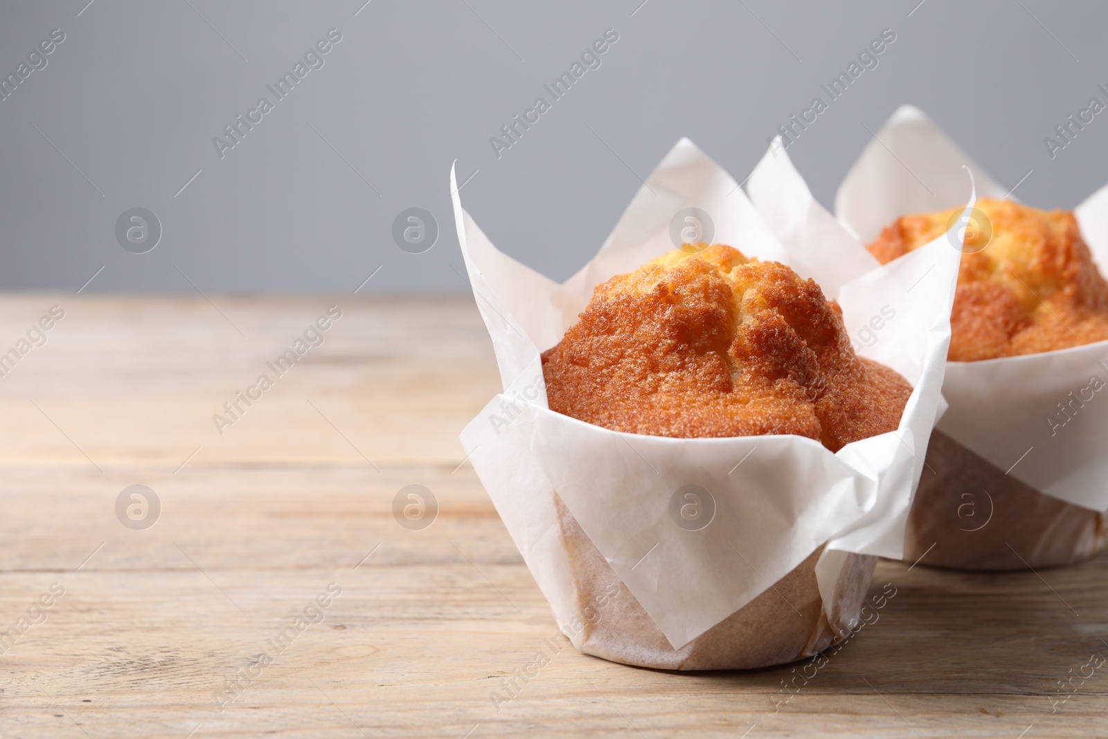 Photo of Delicious sweet muffins on wooden table against grey background, closeup. Space for text