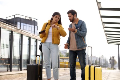 Photo of Being late. Worried couple with suitcases waiting at tram station outdoors
