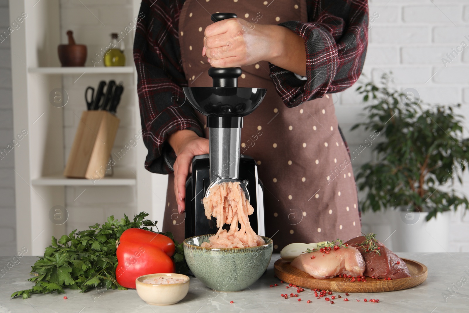 Photo of Woman making chicken mince with electric meat grinder at grey marble table indoors, closeup