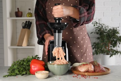 Photo of Woman making chicken mince with electric meat grinder at grey marble table indoors, closeup