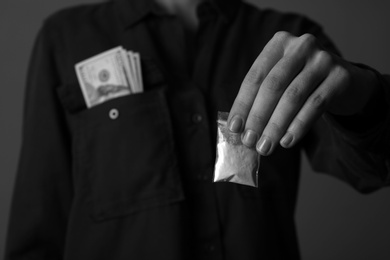 Photo of Drug dealer holding bag with cocaine on dark background, closeup. Black and white effect