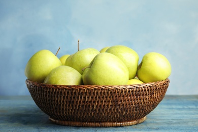 Photo of Wicker bowl of fresh ripe green apples on wooden table against blue background