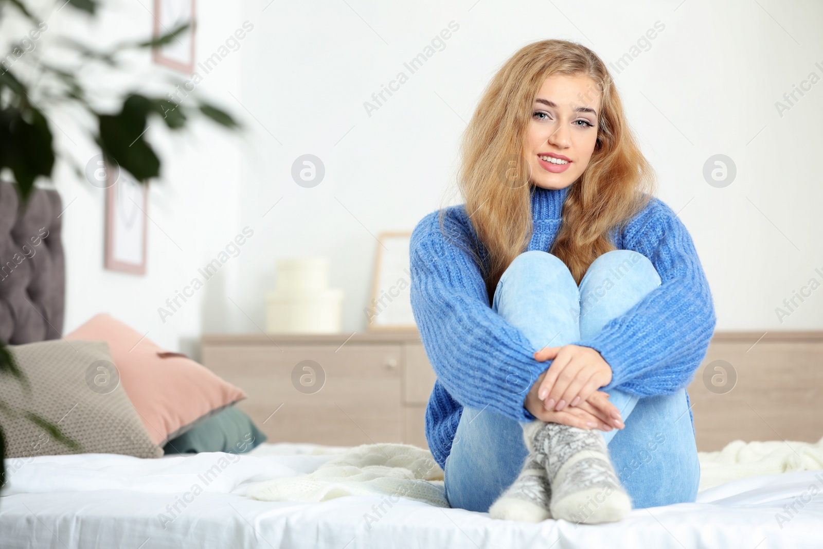 Photo of Beautiful smiling young woman in cozy warm sweater sitting on bed at home. Space for text