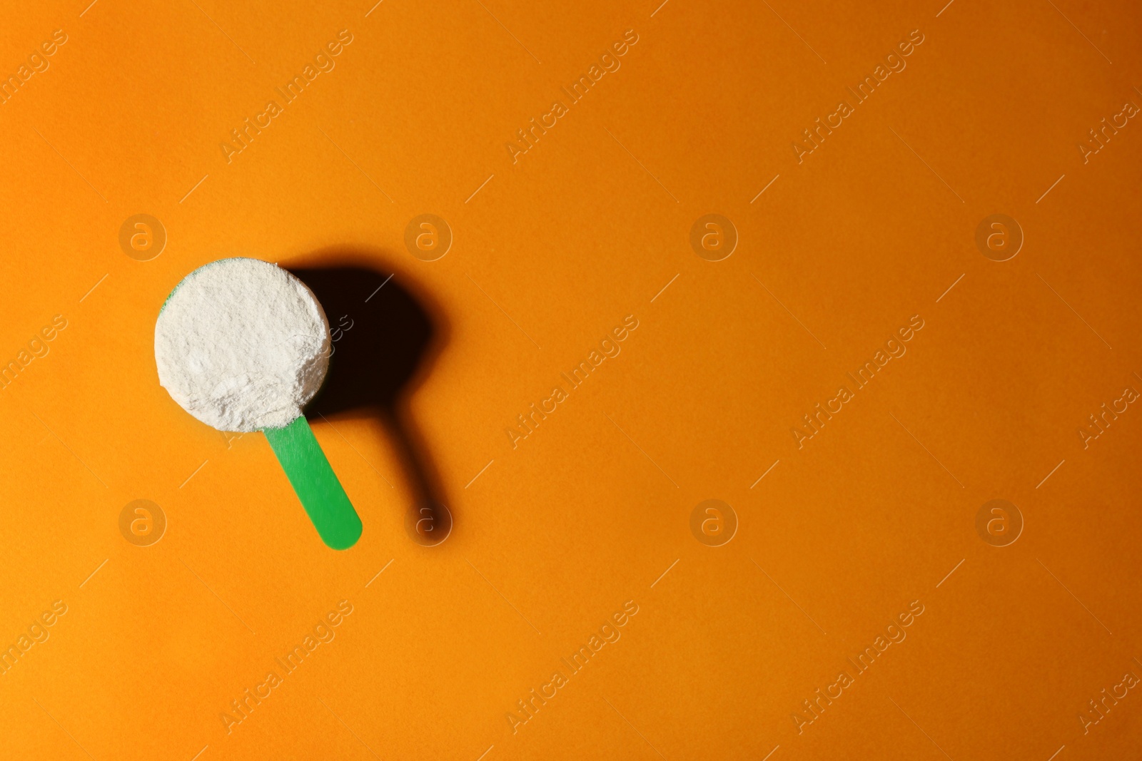 Photo of Scoop of protein powder on orange background, top view with space for text