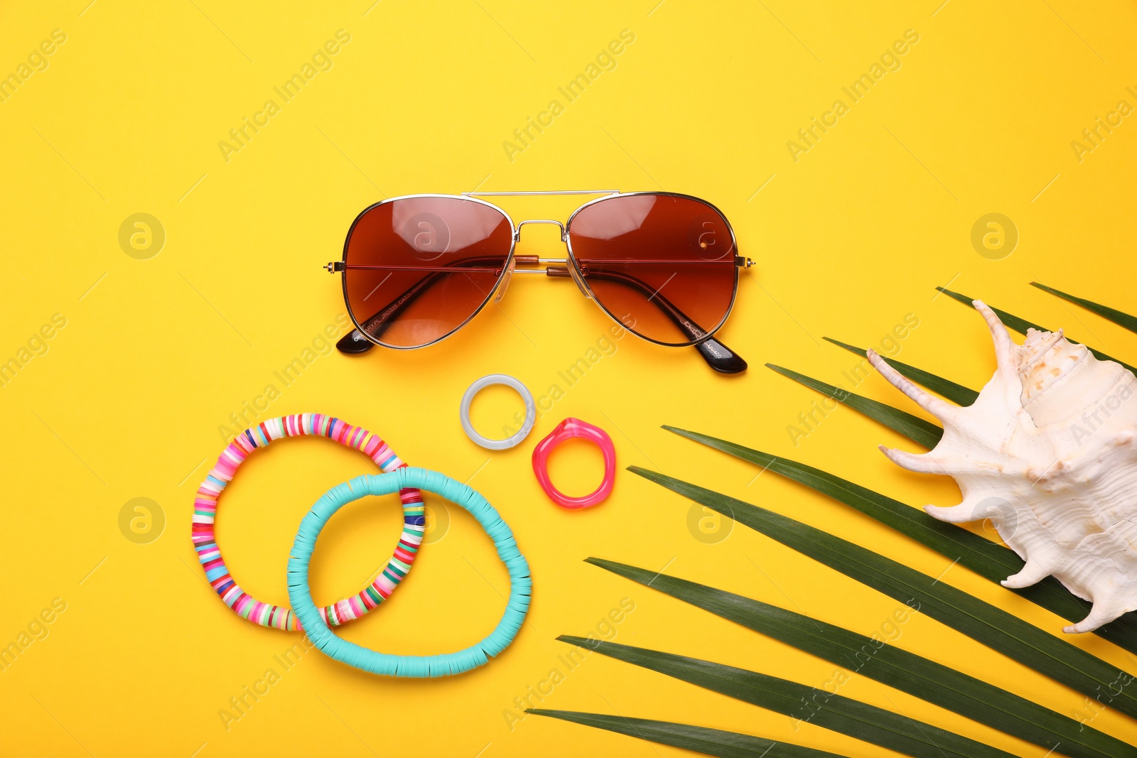 Photo of Stylish sunglasses, bracelets, seashell and rings on yellow background, flat lay