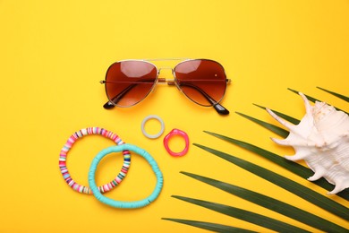 Photo of Stylish sunglasses, bracelets, seashell and rings on yellow background, flat lay