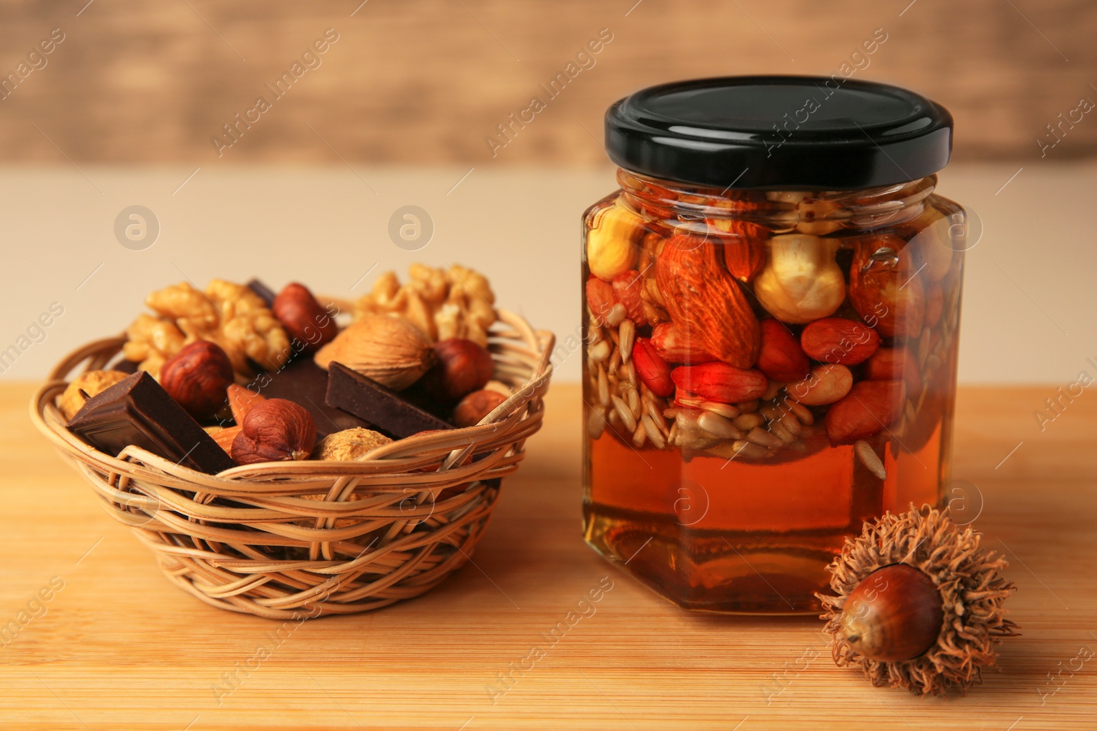 Photo of Different nuts with honey in jar and wicker basket with snacks on wooden table