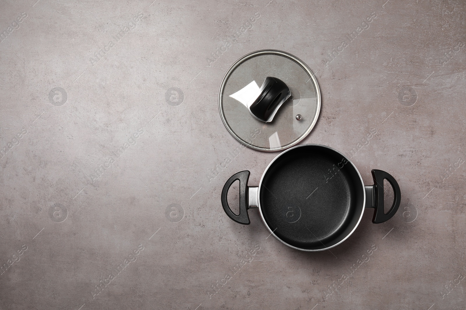 Photo of One empty black pot and glass lid on grey textured table, flat lay. Space for text