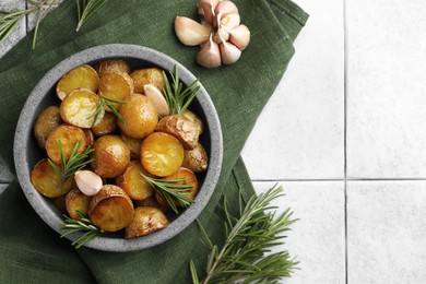 Bowl with tasty baked potato and aromatic rosemary on light tiled table, flat lay. Space for text