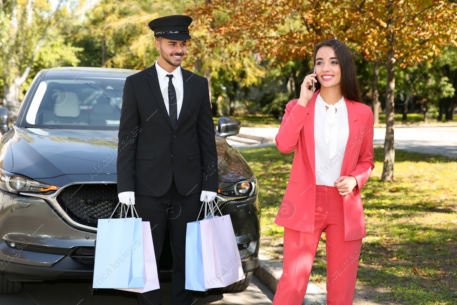 Photo of Handsome driver with shopping bags and young businesswoman near car outdoors