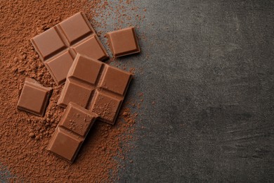 Photo of Delicious milk chocolate and cocoa powder on grey table, flat lay. Space for text