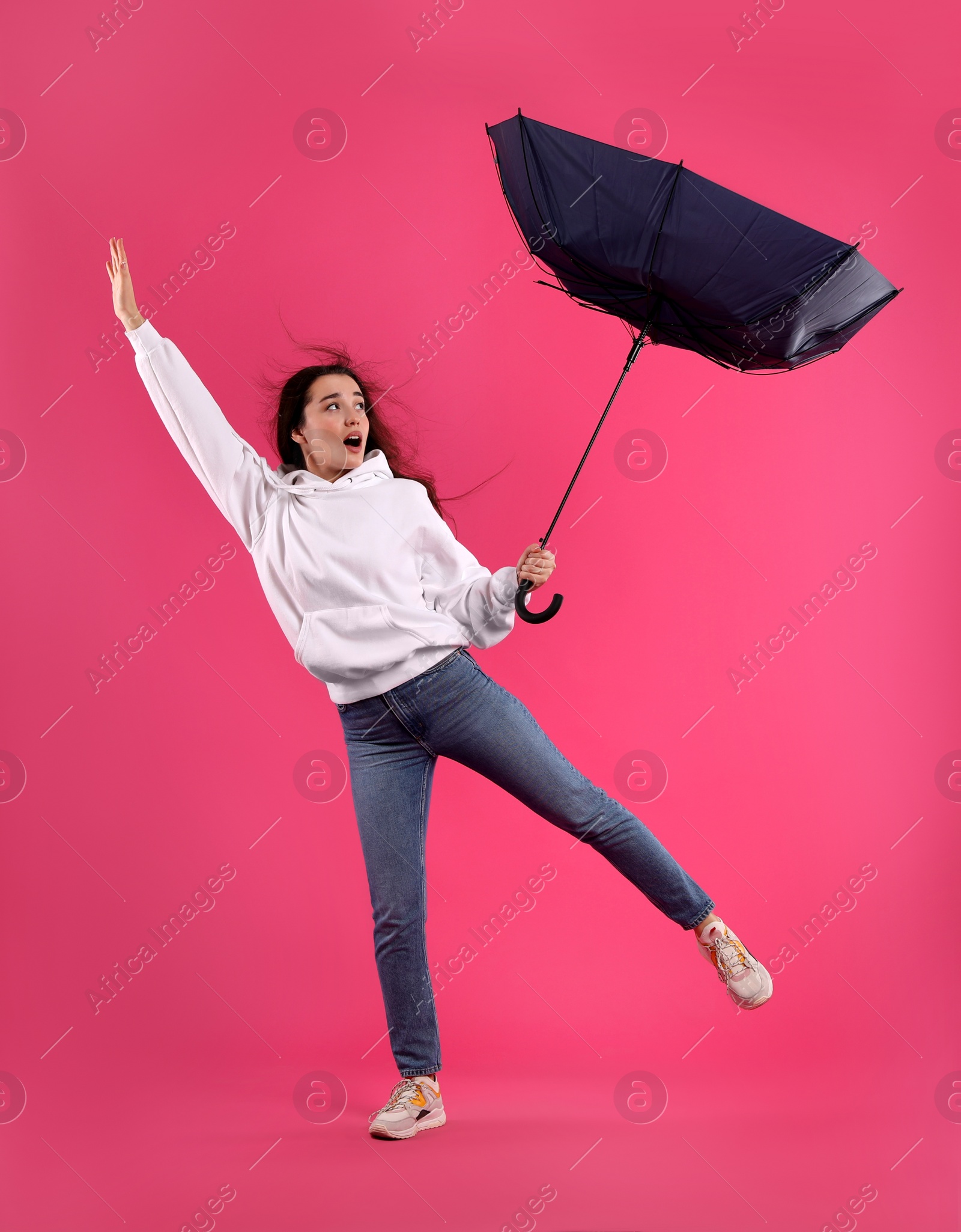 Photo of Emotional woman with umbrella caught in gust of wind on pink background