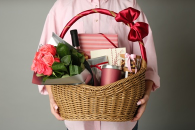 Photo of Woman holding wicker basket full of presents on grey background, closeup