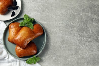 Delicious baked pirozhki and basil on light grey table, flat lay. Space for text