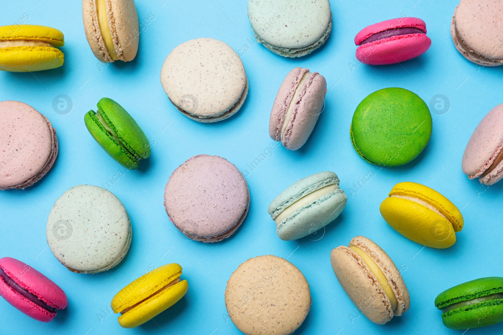 Photo of Delicious colorful macarons on light blue background, flat lay