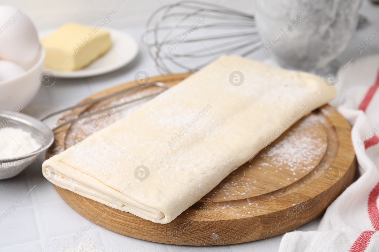 Photo of Raw puff pastry dough on white tiled table, closeup