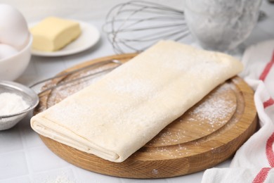 Photo of Raw puff pastry dough on white tiled table, closeup