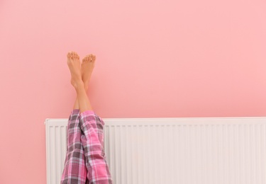 Photo of Woman warming legs on heating radiator near color wall, closeup. Space for text