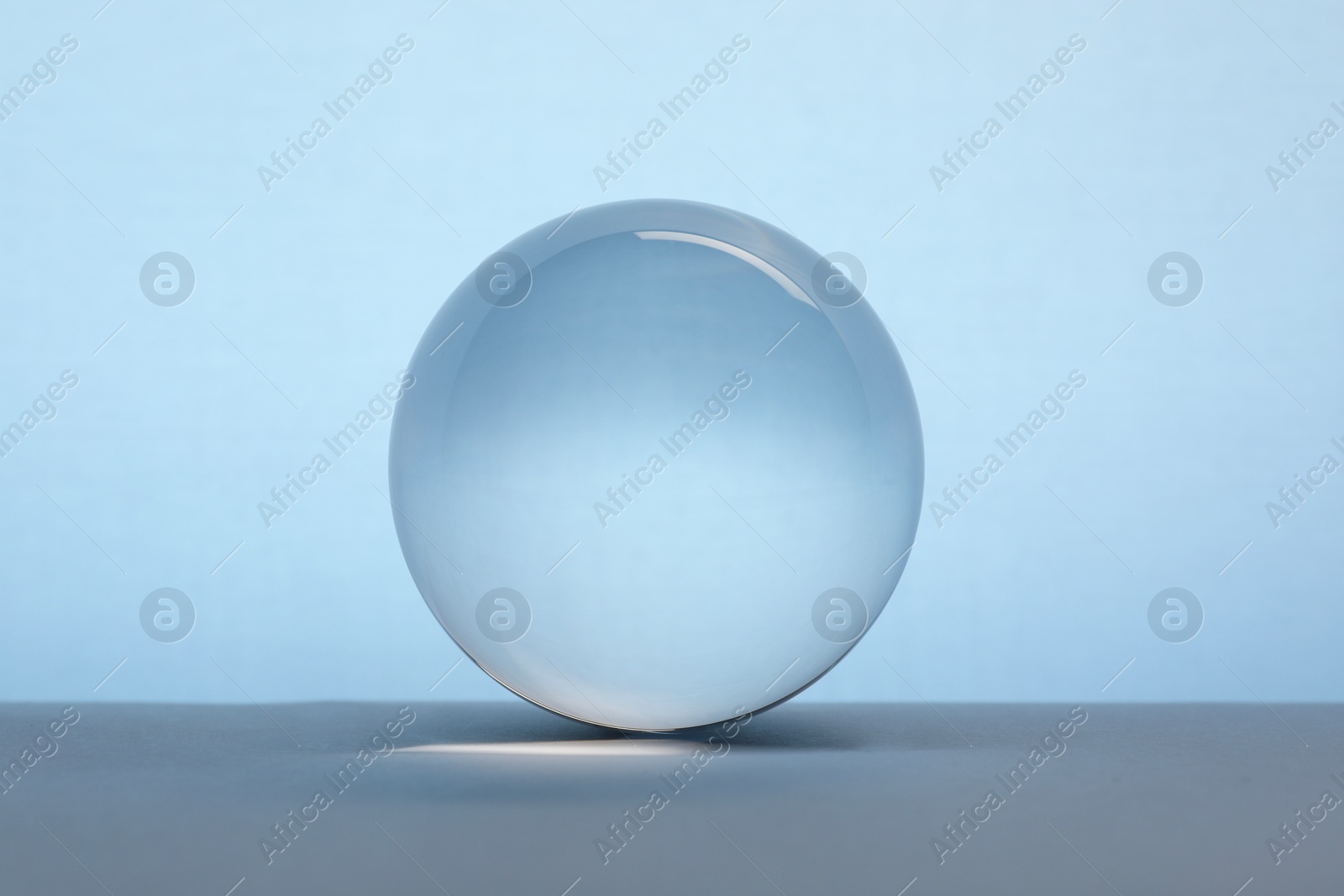 Photo of Transparent glass ball on table against light blue background