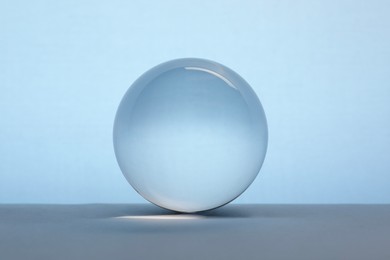 Transparent glass ball on table against light blue background