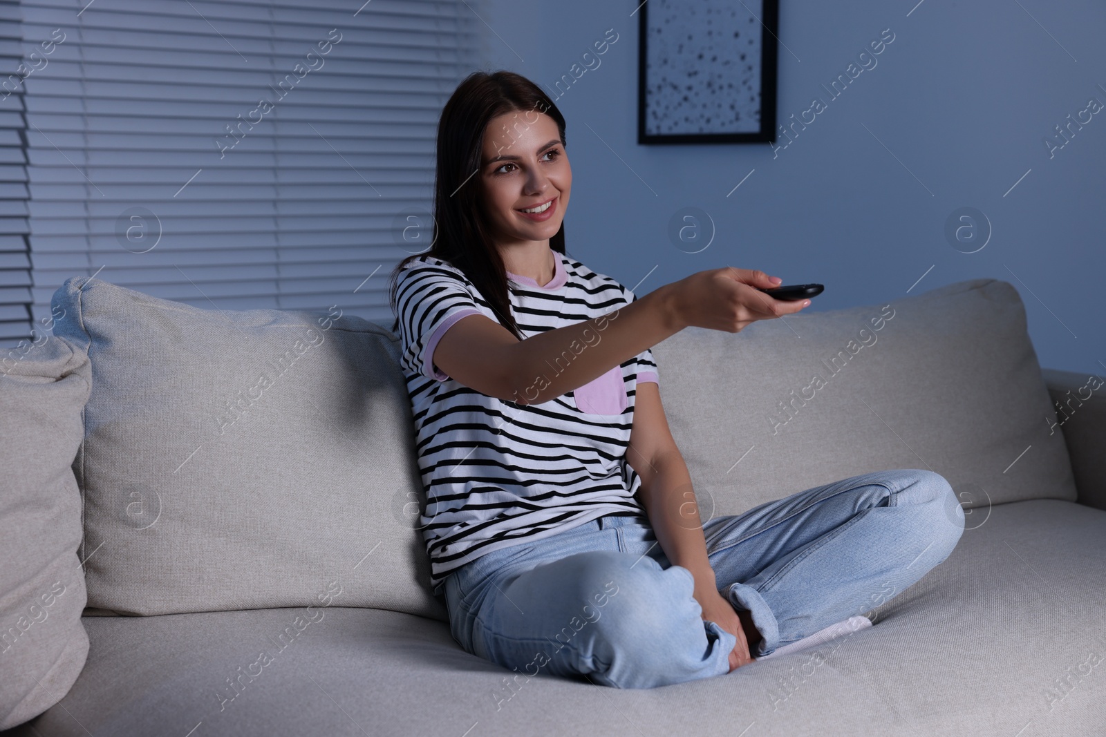 Photo of Happy woman changing TV channels with remote control at home