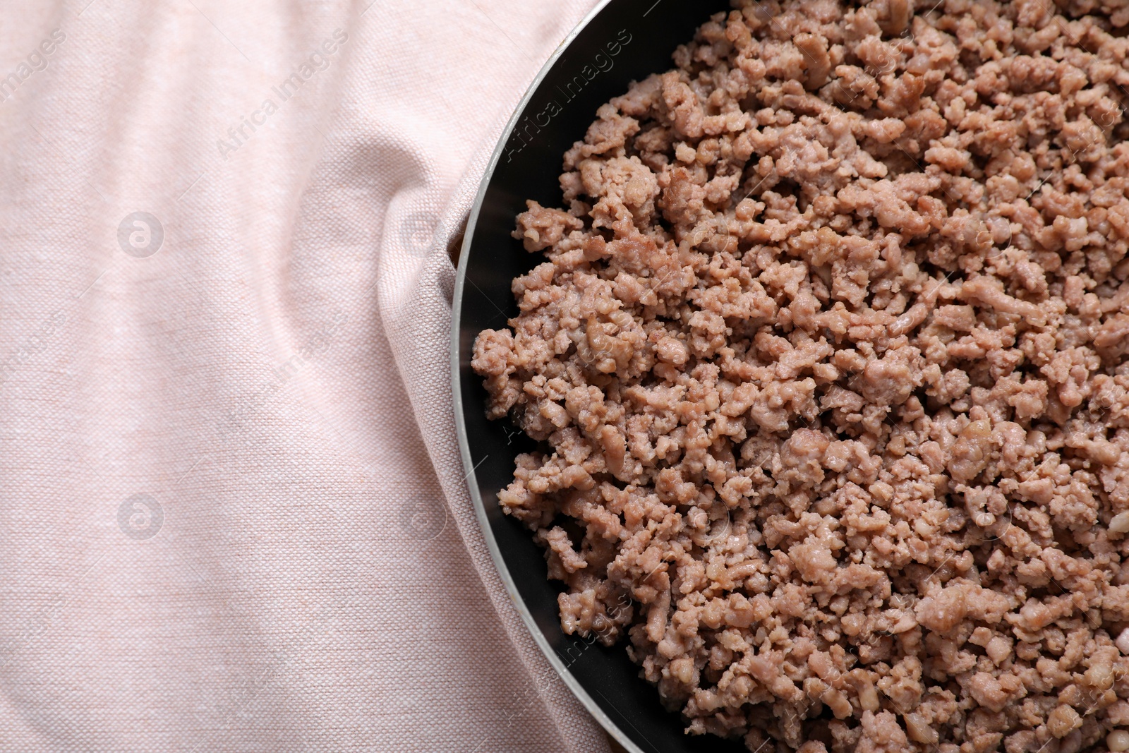 Photo of Fried minced meat in pan on table near kitchen napkin, top view. Space for text