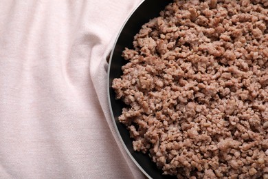 Photo of Fried minced meat in pan on table near kitchen napkin, top view. Space for text